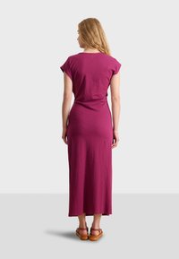 Maxi dress in deep magenta, short cap sleeves, form-fitting design, soft fabric, falls to ankles, paired with brown sandals.
