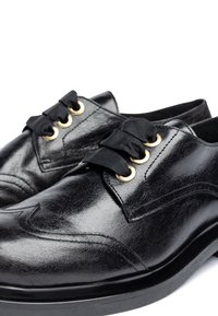 Black leather shoes feature gold eyelets and black ribbon laces. They have a sleek design with embossed detailing and a smooth texture.