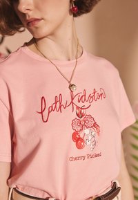 Růžové bavlněné tričko s červeně vyšitým nápisem "Cath Kidston" a grafikou s motivem třešní a květinovými doplňky. Nositelná s náhrdelníkem.