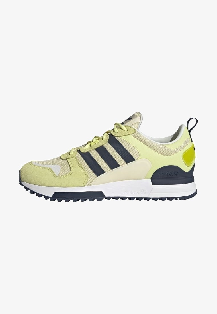Zapatillas verde lima y beige con rayas negras, de material de ante y malla, suela blanca y una suela exterior de goma negra texturizada. Acento notable en el talón.