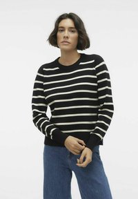 Pull rayé noir et blanc avec un col rond, des manches longues, des poignets et un ourlet côtelés, porté sur un jean bleu. Texture douce, en maille.