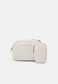 Prošívaná bílá kabelka z umělé kůže se zlatými kovovými doplňky; obsahuje velkou hlavní kapsu a malou kapsu na zip na příslušenství.