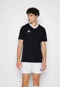Svart idrottströja med vit V-ringning, med en Adidas-logotyp på vänster bröst. Mjuk tyg och korta ärmar.