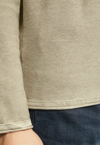 Beige langhals shirt van een textuurstof met een ronde halslijn en geribde manchetten, gecombineerd met donkerblauwe denim jeans.