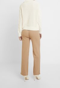 Pull en tricot torsadé crème avec une coupe décontractée, associé à un pantalon large beige. La tenue présente une texture douce et des détails côtelés.