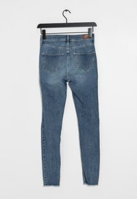 Modré džíny skinny s středně vysokým pasem, obsahující dvě zadní kapsy a třepený lem. Na pasu se nachází kožená nášivka.