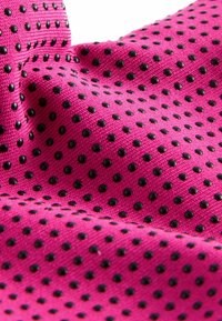 Textil med en ljusrosa bakgrund och en strukturerad yta av svarta upphöjda prickar som är jämnt fördelade.