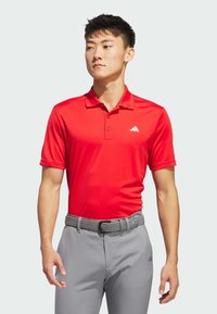 Rød polo skjorte med krave, korte ærmer og Adidas-logo. Sammen med lysegrå bukser og et gråt vævet bælte. Glat stoftekstur.