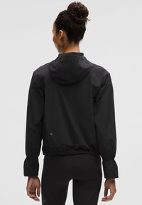 Sort letvægtsjakke med hætte, elastiske manchetter og snøret talje. Glat tekstur, enkel design, ingen synlige mønstre eller hardware.