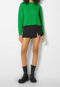 Zelený žebrovaný svetr s nakráceným lemem, doplněný černou mini sukní s bočním rozparkem. Celý outfit doplňují černé robustní kotníkové boty.