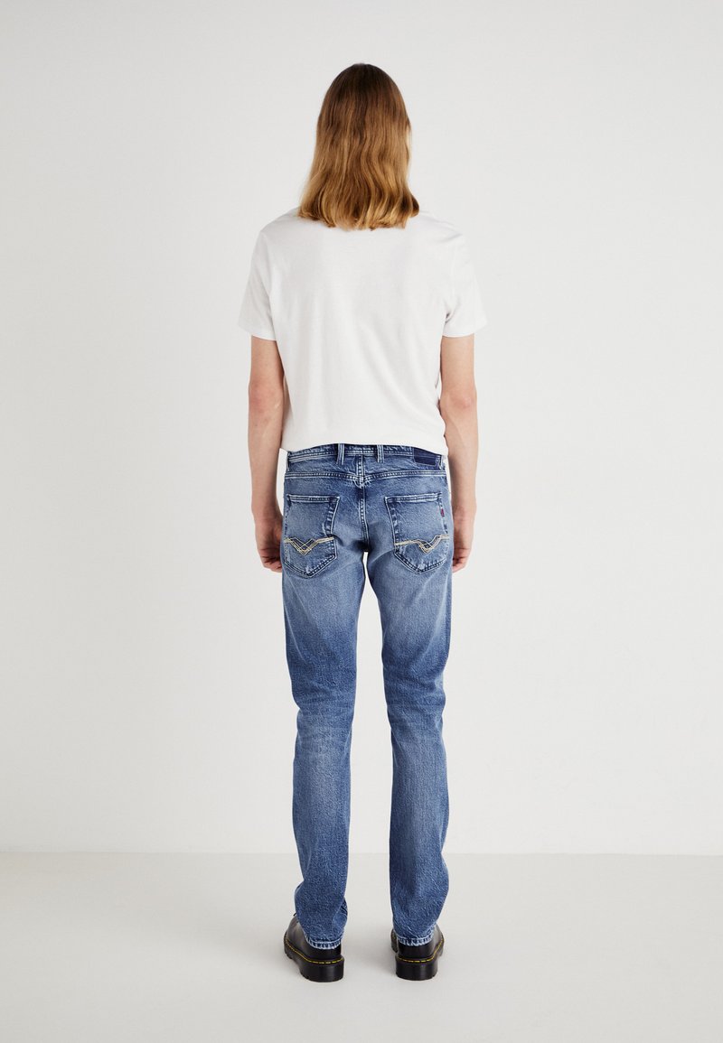 Blauwe denim jeans met een rechte pasvorm, voorzien van twee achterzakken met gele stikselaccenten en een vervaagde wassing. Gecombineerd met een wit t-shirt.