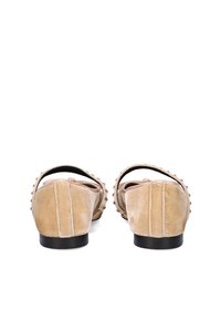 Bailarinas de ante beige con punta redondeada, que cuentan con una correa trasera y tachuelas metálicas decorativas a lo largo de los bordes. Textura suave y diseño minimalista.