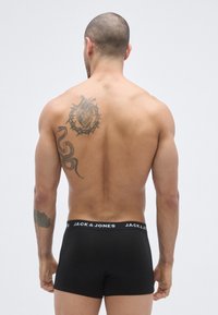 Svarta boxerbriefs med en kontrasterande logotyp på midjebandet, visade på en bar rygg. Synlig hjärt- och ormtatuering på vänster axel.