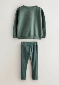 Tumši zaļš džemperis ar ribotām piedurknēm un apkakli, pārī ar atbilstošām ribotām legingām. Mīksta tekstūra un pieguļošs dizains komfortam.