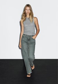 Gray sleeveless top paired with high-waisted, loose-fitting gray jeans. Model wears black flip-flops. Simple, minimalistic design on white background.