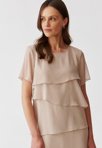 Beige kerroksellinen yläosa lyhyillä hihoilla, jossa on pystysuora ribbikuvio ja pyöreä pääntie, luoden pehmeän ja virtaavan siluetin.