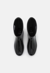 Bottes en caoutchouc noir avec une finition lisse, un bout rond et un tige de hauteur moyenne. Intérieur doublé et étiquette de taille visible à l'intérieur.