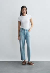 Λευκή κοντομάνικη ριγέ μπλούζα συνδυασμένη με ανοιχτομπλε ίσια τζιν και καφέ επίπεδες σανδάλια με ταμπόν και υφασμάτινες λωρίδες.