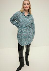 Camicetta a maniche lunghe in teal con stampa paisley, tasca sul petto, orlo curvo. Abbinata a leggings in ecopelle neri e stivaletti cowboy neri.