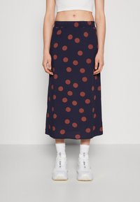 Larga falda azul marino con grandes lunares color óxido, cintura elástica y tejido fluido, combinada con zapatillas blancas y calcetines.