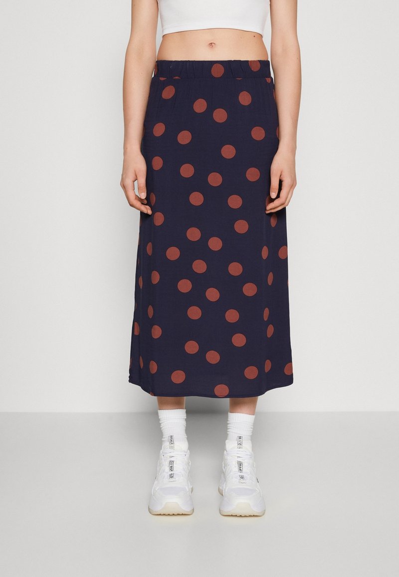 Larga falda azul marino con grandes lunares color óxido, cintura elástica y tejido fluido, combinada con zapatillas blancas y calcetines.