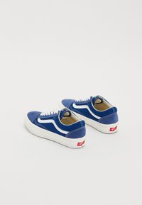 Baskets en daim bleu avec des accents blancs, design classique à lacets, et une semelle en caoutchouc blanche. Présente un logo rouge sur le talon.