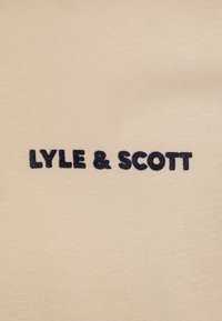 Beżowy materiał z czarnym haftowanym napisem "LYLE & SCOTT" wyśrodkowanym w obrazie.