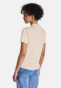 Beige kortärmad pikétröja med en mjuk textur, med en klassisk krage och slim fit, kombinerad med ljusblå denimjeans.