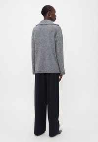 Maglione grigio a maglia con un ampio colletto e spacchi laterali, abbinato a pantaloni neri a vita alta e dal taglio loose. Texture liscia.