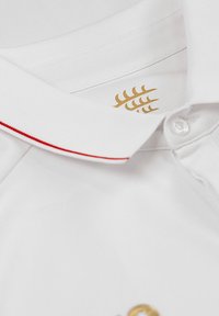 Polo bianco con una striscia rossa sul colletto, caratterizzato da un logo dorato e dettagli dei bottoni. Realizzato in un tessuto liscio e strutturato.