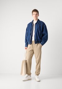Denim bomberjakke i mørkeblå, hvit t-skjorte, beige joggebukser og hvite sneakers. Bærer en beige tote bag.