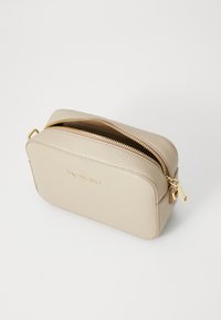 Trousse de maquillage en cuir beige avec fermeture éclair dorée, de forme rectangulaire, surface texturée, et nom de marque en relief à l'avant.