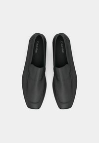 Μαύρα παντόφλια με λεία δερματίνη εξωτερικά. Μινιμαλιστικός σχεδιασμός με στρογγυλή μύτη και κεντητές ραφές. Το όνομα της μάρκας είναι τυπωμένο εσωτερικά.