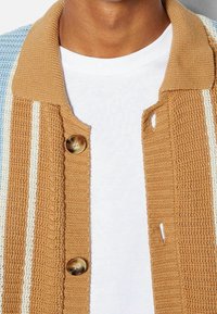 Knit cardigan with a tan collar and buttons, featuring blue, cream, and tan striped patterns on a textured fabric.