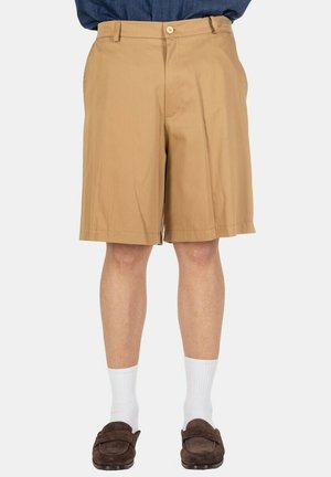 Uomo che indossa pantaloncini beige fino al ginocchio, calzini bianchi, mocassini marroni e camicia blu infilata.