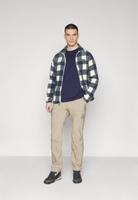 Fleece jacket with navy and cream check pattern, navy t-shirt, beige cargo pants, and black hiking shoes, standing against a plain background.