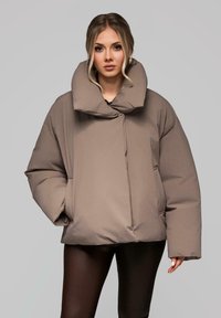 Puchowa taupe kurtka z oversize kołnierzem, z przodu zapięciem i dużymi kieszeniami. Charakteryzuje się gładką fakturą i luźnym krojem.