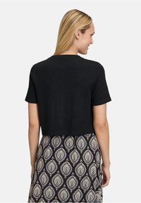 Schwarzes Cropped-Top aus strukturiertem Strickmaterial mit kurzen Ärmeln, kombiniert mit einem gemusterten Rock mit einem Blattmotiv in Beige und Marineblau.