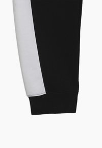 Svarta träningsoveraller med en vit sidopanelsdetalj, tillverkade av mjuk bomullsmaterial, med ribbad midja och slät yta.