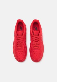 Crvene Nike Air Force 1 tenisice s glatkim kožnim gornjištem, perforiranim prednjim dijelom i odgovarajućim vezicama. Sadrže logotip na jeziku i ulošku.