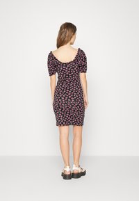 Vestido floral com mangas bufantes, fundo preto e flores rosas. Silhueta ajustada, comprimento abaixo do joelho, com costas largas e em forma de colher.