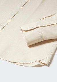 Camisa botón de color beige claro con una textura suave, presenta un puño doblado y un dobladillo curvo, hecha de un tejido transpirable.