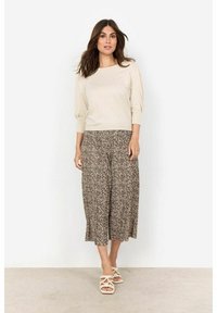 Krémový top s nadýchanými rukávy v kombinaci s širokými leopardími culottes. Oblečení se vyznačuje uvolněným střihem a měkkými materiály, doplněné o sandály na pásky.