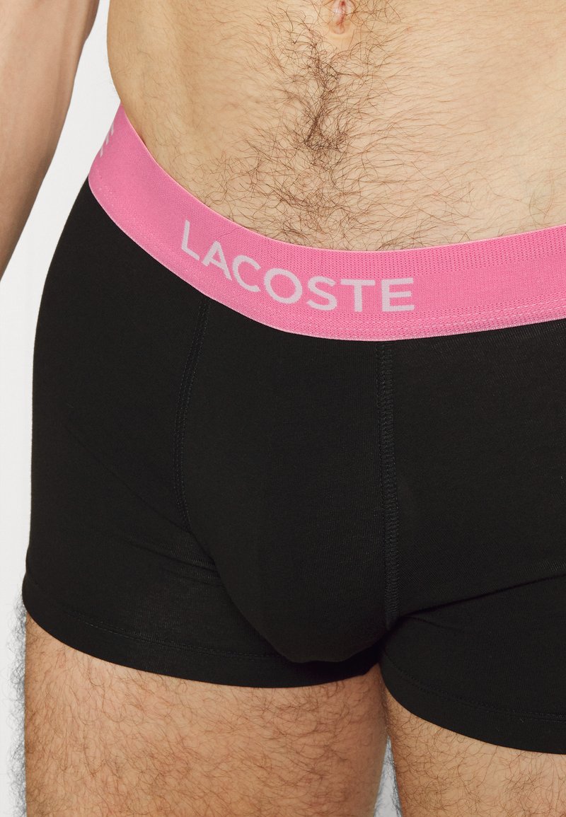 Zwarte katoenen boxershorts met een roze elastische tailleband waarop "LACOSTE" in het wit is gedrukt, met een gladde textuur en een aansluitend ontwerp.
