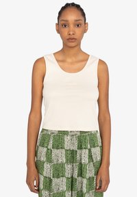Hvid ribbet tanktop med en udringet hals, bæres med en grøn og hvid mønstret nederdel med et ternet design. Enkel og tætsiddende silhuet.
