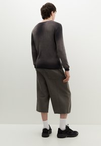 Donkergrijze gebreide trui met lange mouwen. Losse olijfgroene shorts met zijzakken. Zwarte sneakers en witte sokken maken de outfit compleet.