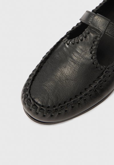 Pantof de piele neagră cu un design cusut împletit de-a lungul marginii, cu o decupare lângă gleznă. Textură netedă cu un vârf rotunjit.