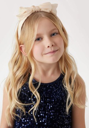 Navy sequin dress with a round neckline, paired with a light beige satin headband featuring a large bow detail. Long wavy blonde hair.