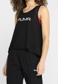 Svart ärmlös crop top med rundad halsringning, prydd med en vit "PUMA"-logotyp framtill. Bärs med svarta byxor.