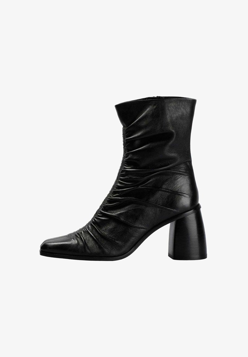 Bota de tobillo de cuero negro con textura recogida, punta afilada y tacón grueso. El diseño presenta un acabado liso y una construcción minimalista.